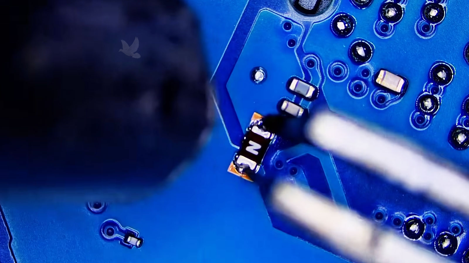 Damaged N-marked fuse held with tweezers while hot air releases it from the circuit board
