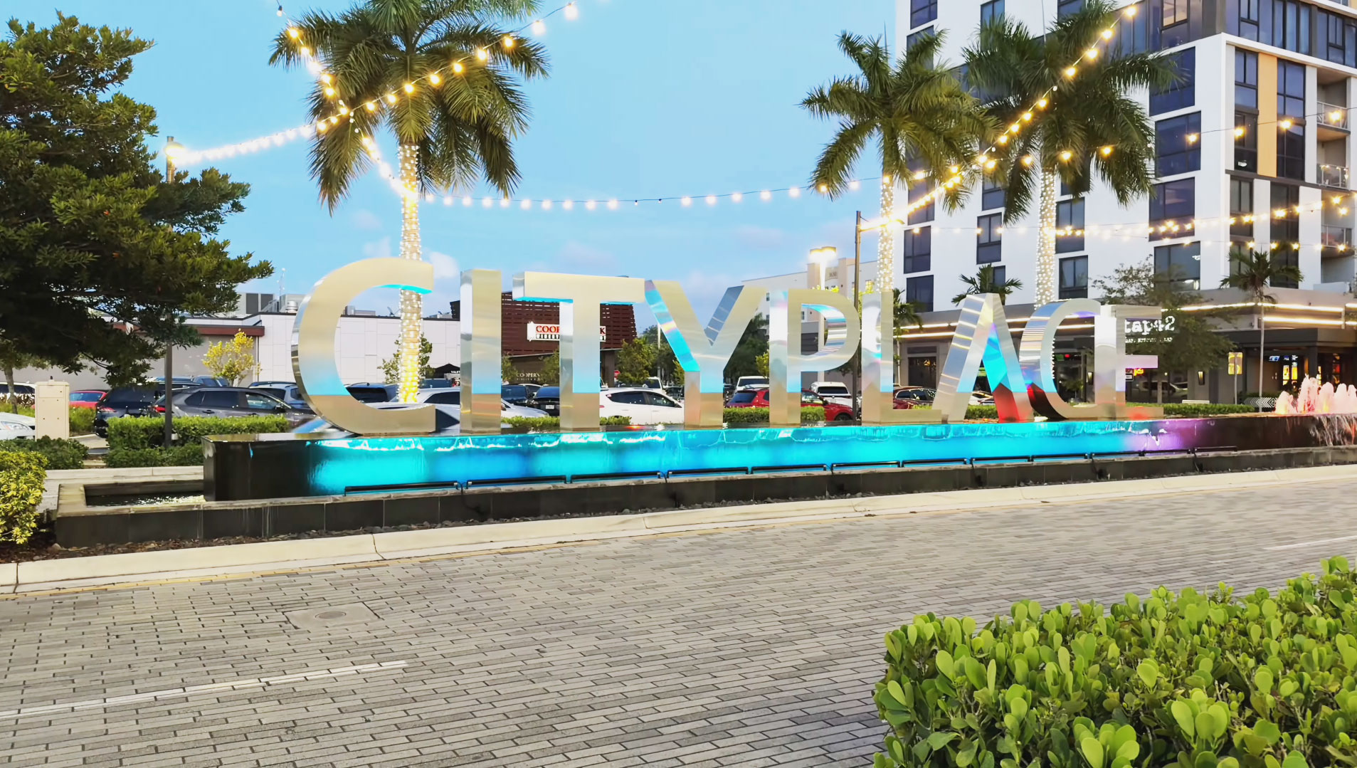 Illuminated CityPlace Doral sign with blue lights, palm trees, and decorative tree lighting at dusk