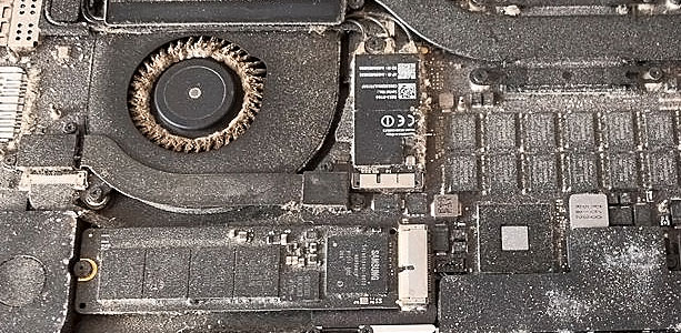 MacBook Air interior covered with heavy dust and debris concentrated around the cooling fan