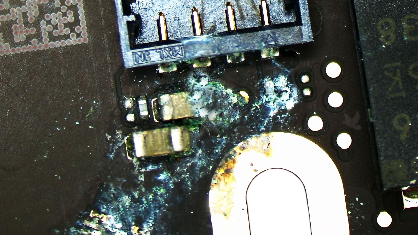 MacBook-Air-Liquid-Damage-Repair-with-Two-Corroded-Capacitors MacBook Air liquid damage repair with two corroded capacitors behind a motherboard connector requiring replacement