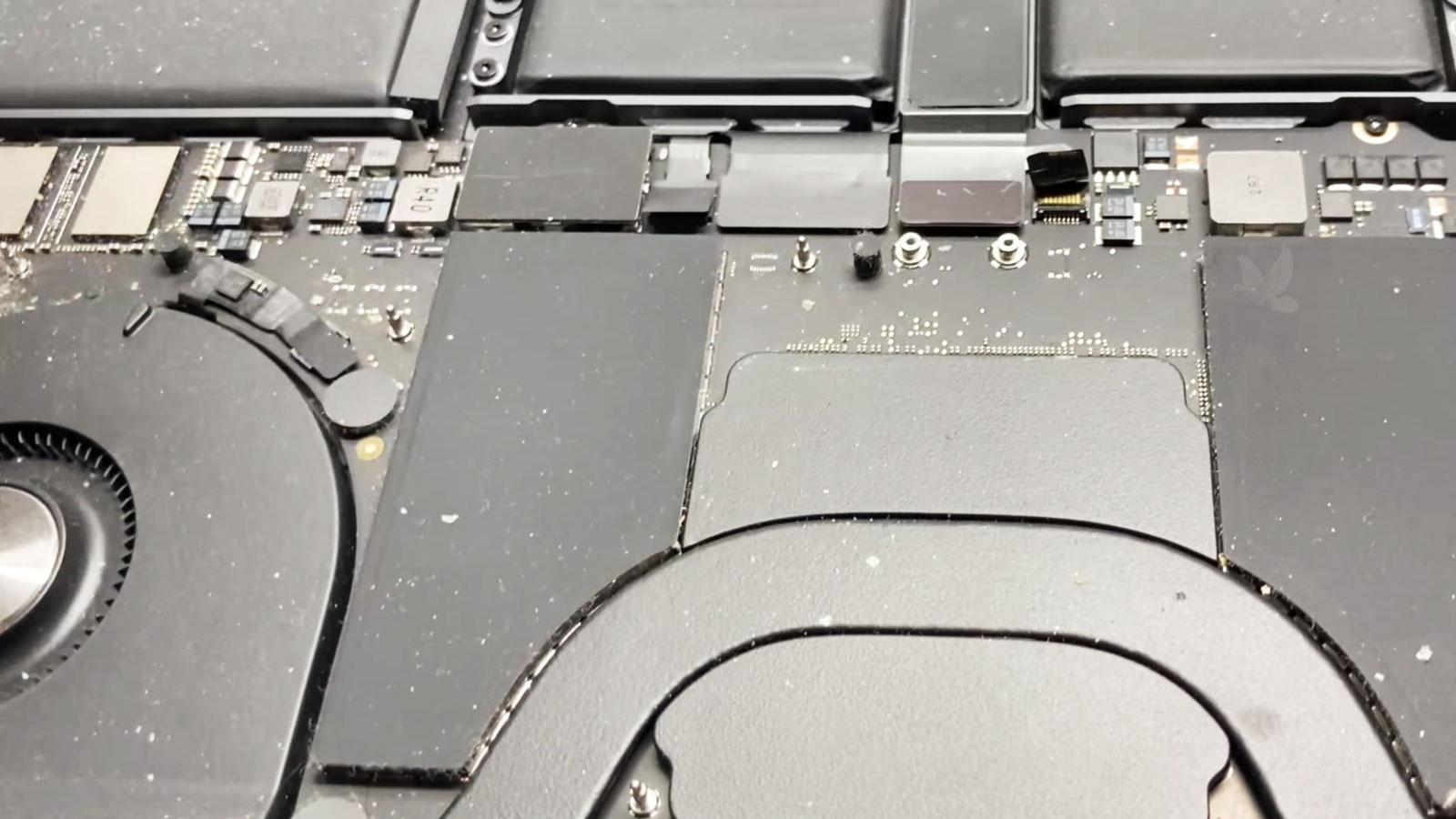 Dust and debris buildup inside an open MacBook Pro around the fan, heatsink, and motherboard