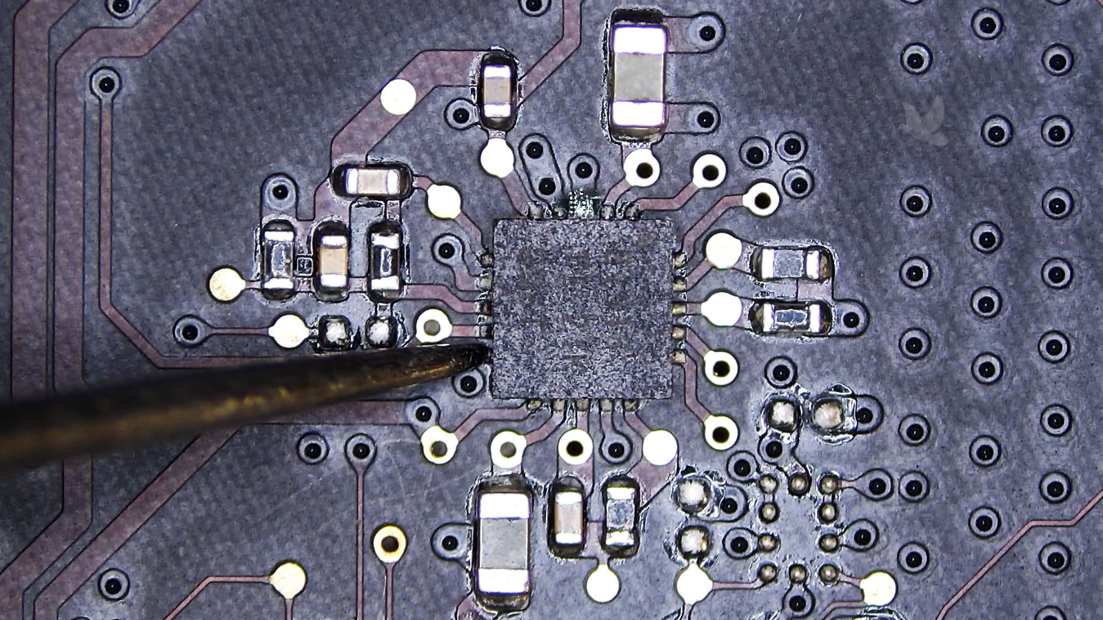 MacBook Pro logic board IC being tested with corrosion visible on two pins