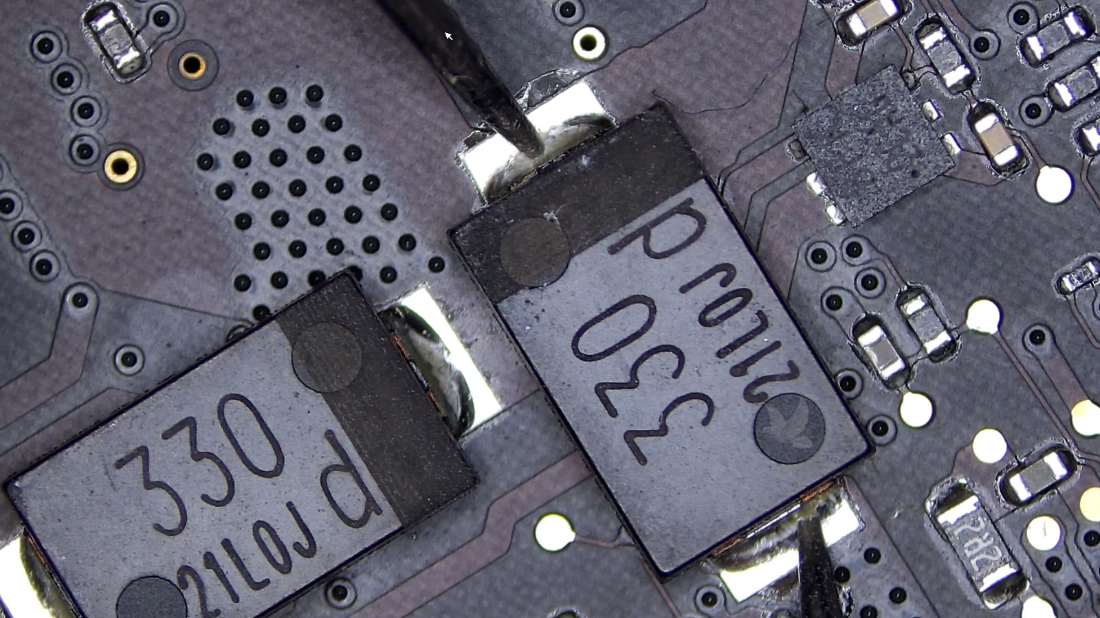 SMD capacitor marked 330 being measured on a MacBook Pro logic board during diagnostics