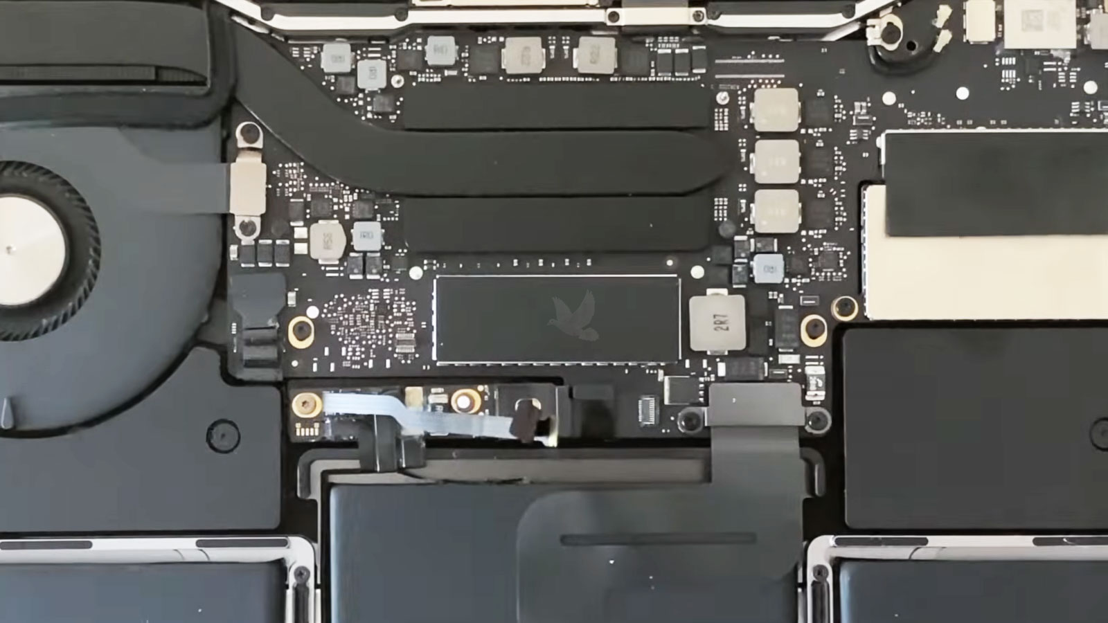 MacBook Pro with back cover removed showing the removable SSD secured by a metal shield and two screws