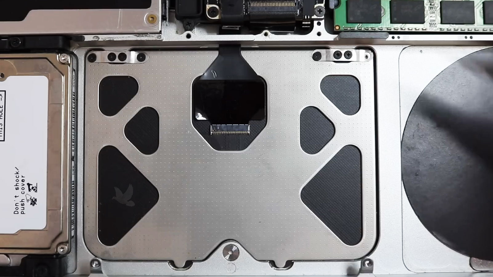 MacBook Pro trackpad exposed from inside with flex cable and mounting screws visible
