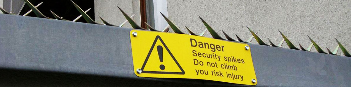Metal anti-climb security spikes above a warning sign stating danger, do not climb, risk of injury