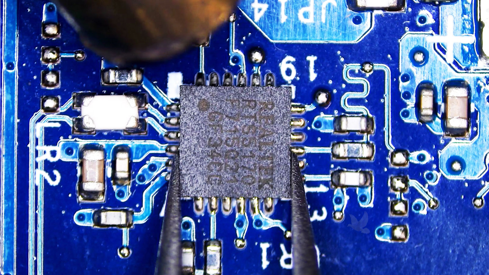 Realtek-IC-Removal-During-Laptop-Motherboard-Repair Damaged Realtek IC held with tweezers and prepared for removal with a hot air rework station