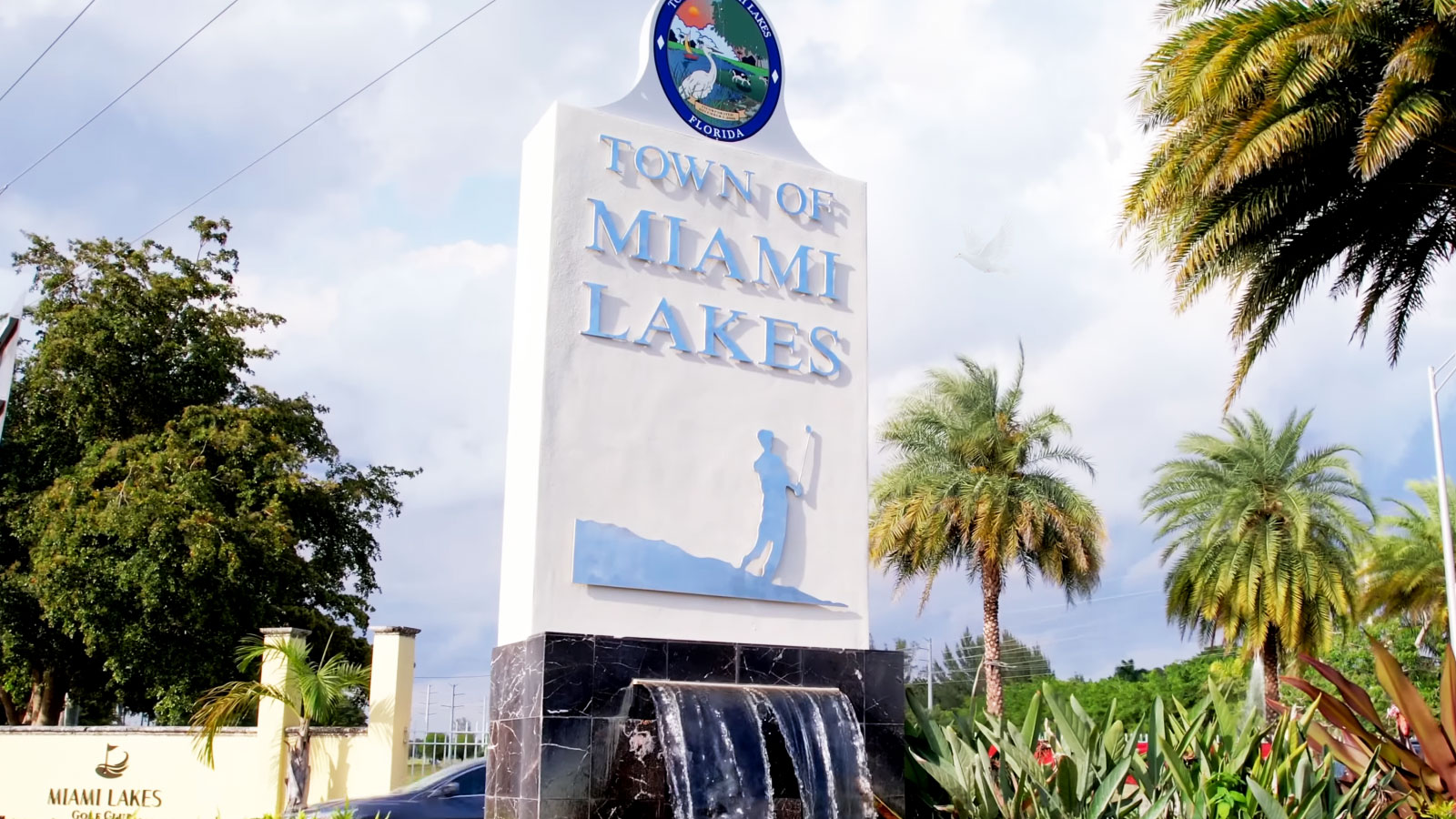 Town of Miami Lakes sign with a small waterfall and a golfer holding a golf club