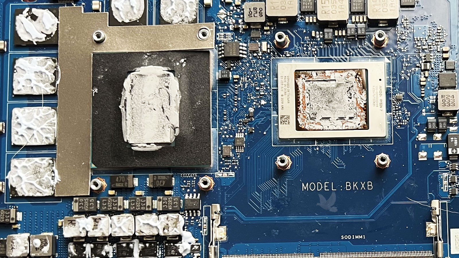 BKXB laptop motherboard showing deteriorated thermal pads around the graphics chips, memory components, and surrounding coils, requiring replacement to restore proper thermal contact.