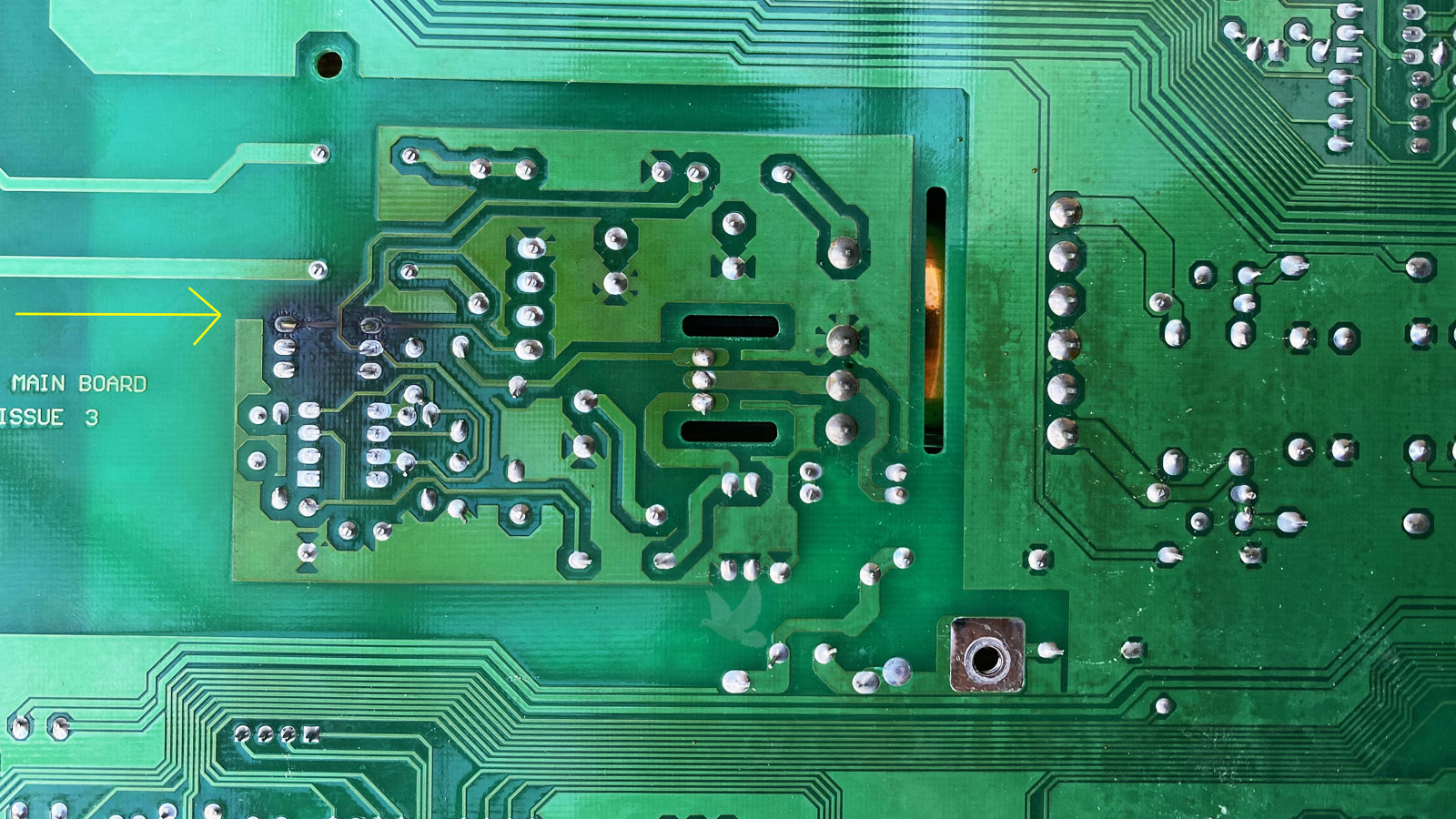 Green circuit board showing severe heat damage, with a large blackened section where intense overheating has caused visible discoloration.