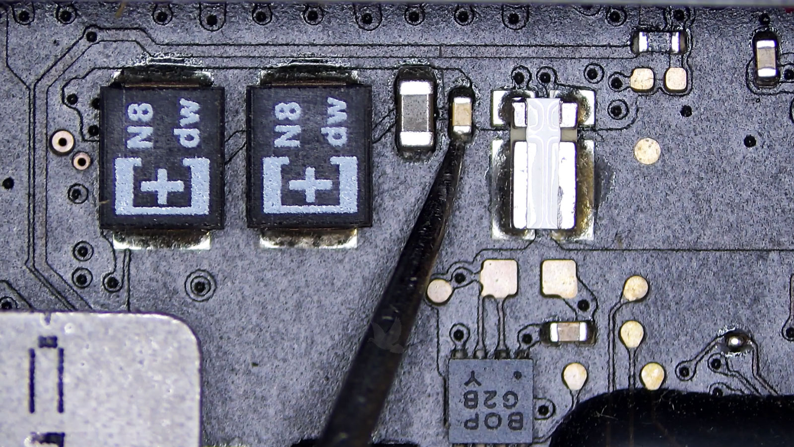 Damaged small capacitor positioned between larger capacitors on a circuit board