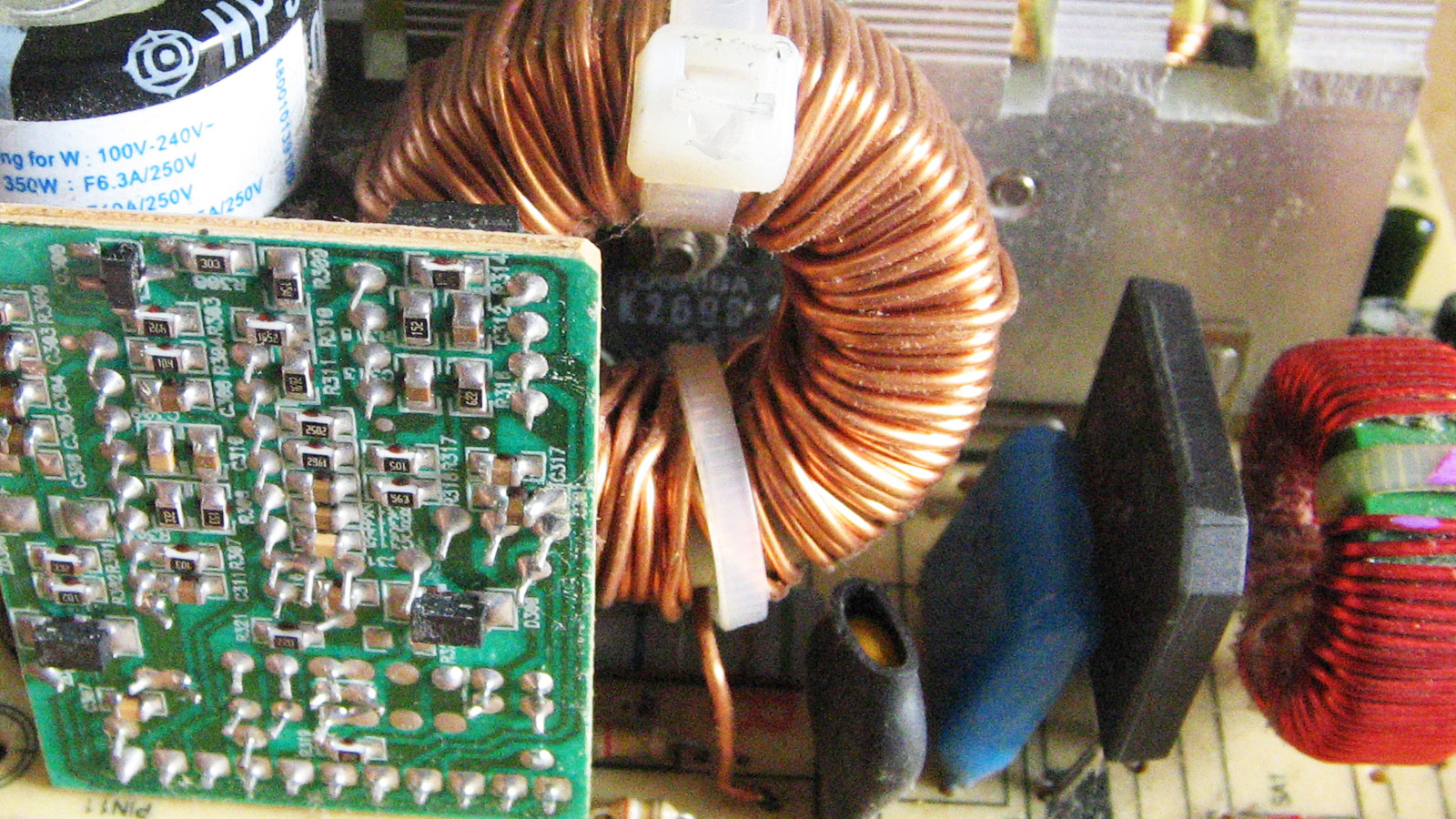 Circuit board showing a damaged transistor behind a power coil and a faulty bridge rectifier beside two coils, with both components requiring replacement.