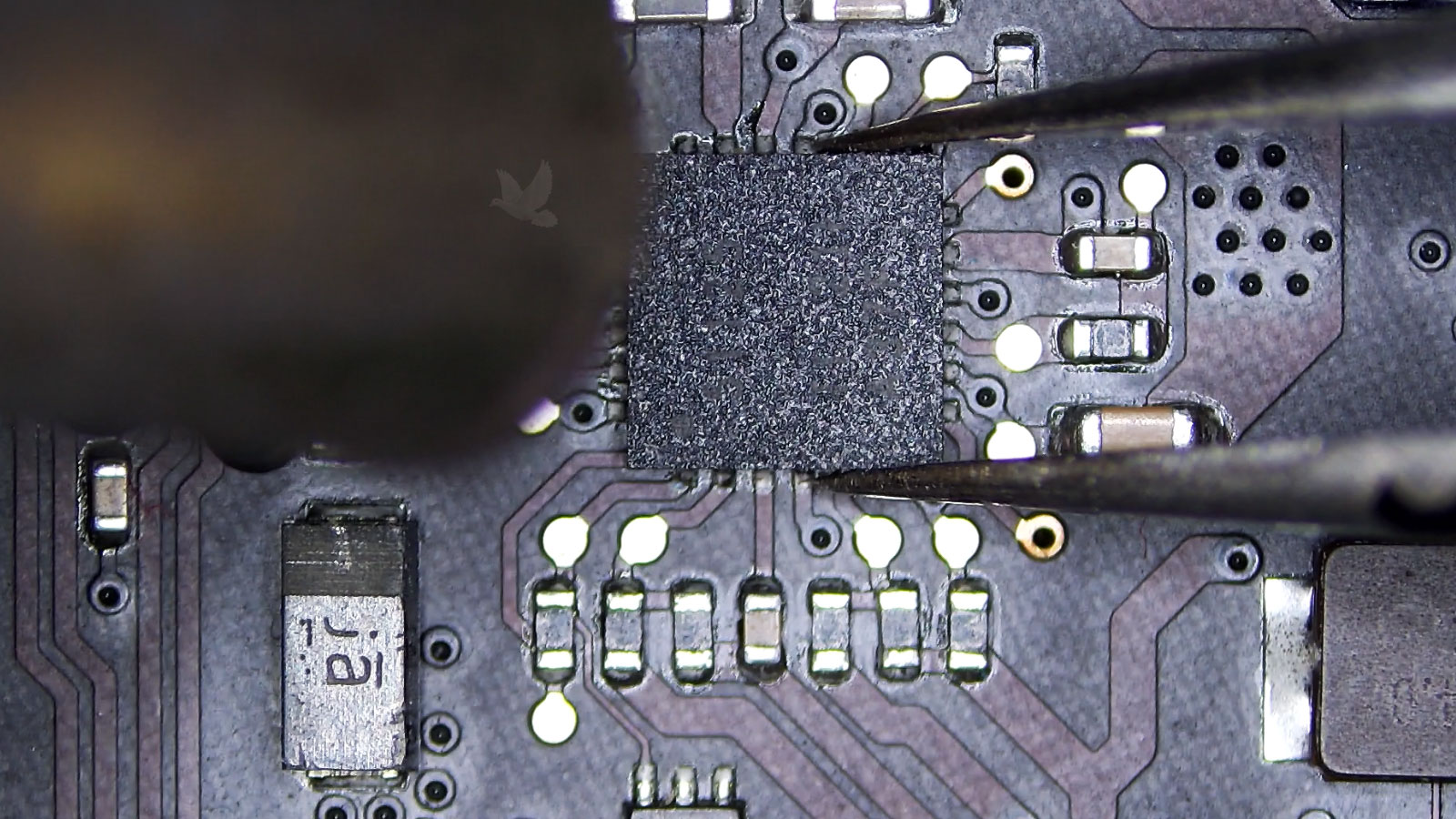 Shorted IC near capacitors and resistors being held with tweezers during hot air removal